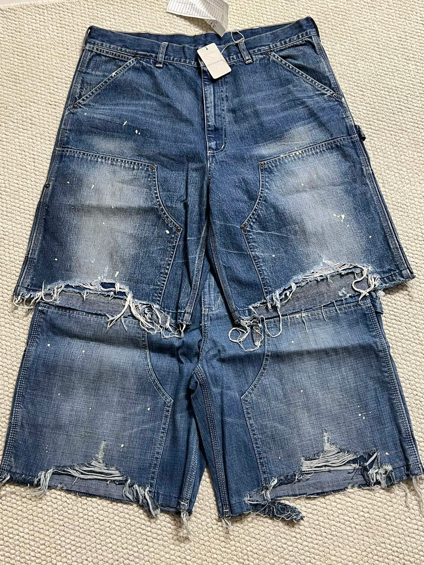 SAINT Mxxxxxx DOUBLE KNEE SHORTS/BLU Knee patches splashed with ink and water-splashed denim shorts. Denim blue S-XL. Custom-woven and dyed denim fabric with clear texture. Heavy-wash water-fading treatment to create local mottled fading/hole effects. Artificial distressing to simulate natural wearing marks. VINTAGE sense. Original consistent damage treatment. Hand-splashed ink and paint. Original consistent wash mark/pocket mark. Double knee patch. Rivet reinforcement. Improve functionality while enhancing design